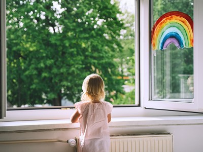 Punčka gleda skozi odprto okno na katerem je narisana mavrica