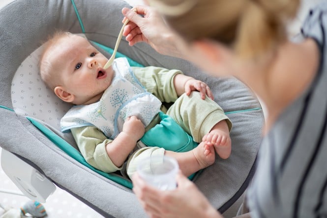 Mama z žličko hrani dojenčka v otroškem stolu