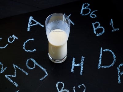 Kozarec mleka na temni podlagi z napisanimi posameznimi vitamini in minerali