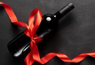 Temna vinska steklenica obdana z rdečo pentljo na temni podlagi