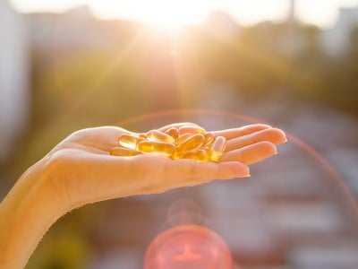 Ženska roka drži vitamin D kapsule obsijane s soncem