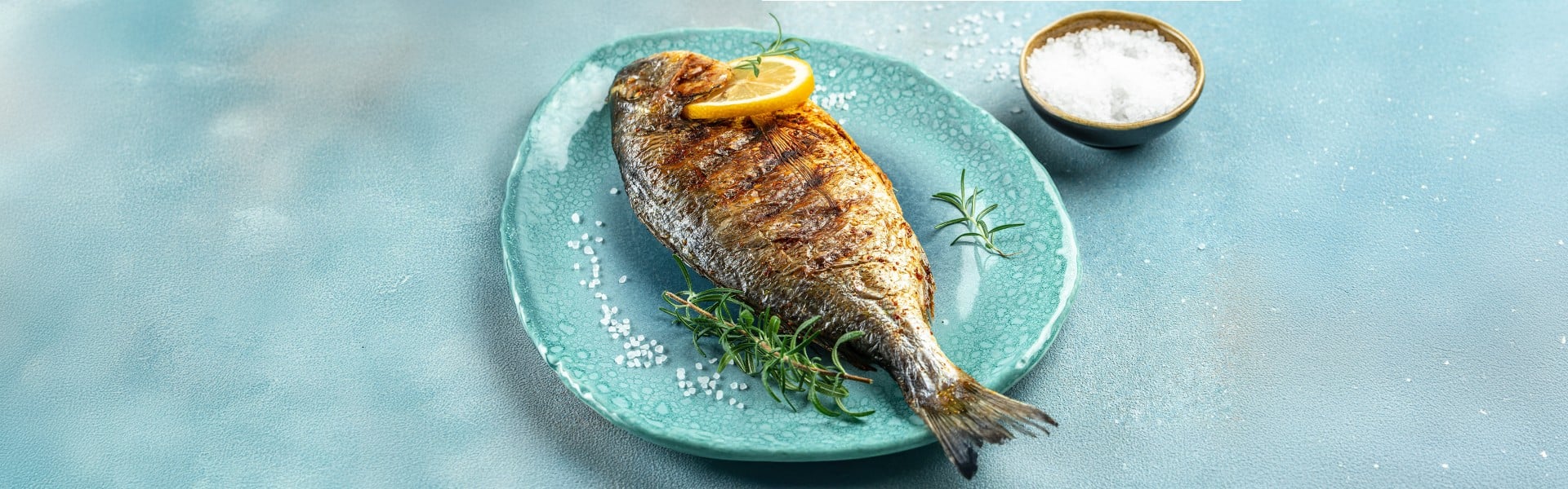 Na žaru pečena orada, postrežena na modrem krožniku