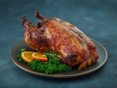 Na krožniku postrežena pečena gos z zelišči in rezinami pomaranče
