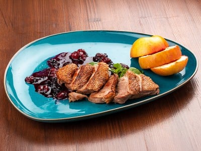 na krožniku postrežena gosja prsa z brusnično omako in jabolki