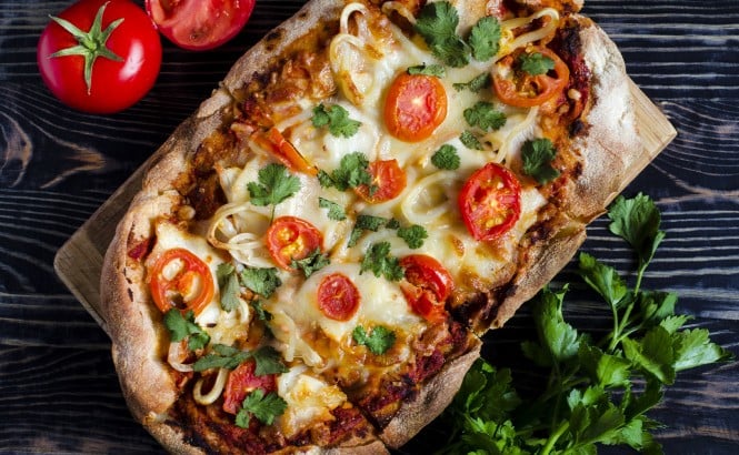 Pinsa obložena s paradižniki in mozzarello na temni podlagi