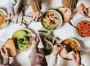 Ljudje za mizo jedo različne kremne veganske juhe