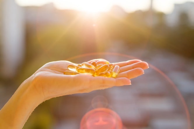 Roka drži kapsule vitamina D, osvetljene s soncem