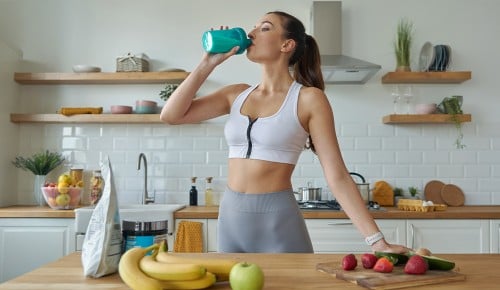 Proteini – samo za fitnes navdušence ali za vsakogar? Ženska v športnih oblačilih pije proteinski napitek