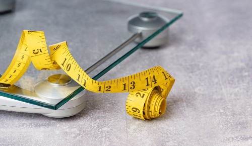 yellow tape measure on top of glass bathroom weighing scale on blue. Front view copy space. Healthy lifestyle, weight losing management and hydration concept banner