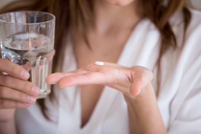 Ženska v eni roki drži tableto in v drugi kozarec vode